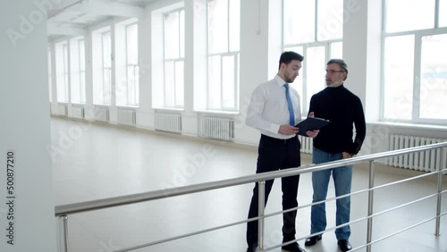 Businessman is talking to realtor about terms renting an office space, front view. Real estate agent with tablet in hands discusses with client terms of lease of premises
