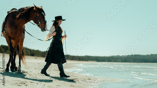 Portrait of a Beautiful Caucasian Hippie Woman Walkingwith a Gorgeous Brown Horse in a Blue Sky and Sea Background at an Isolated Beach Area. photo