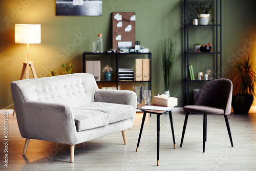 Empty chair and sofa iin front of small table in office of psychologist