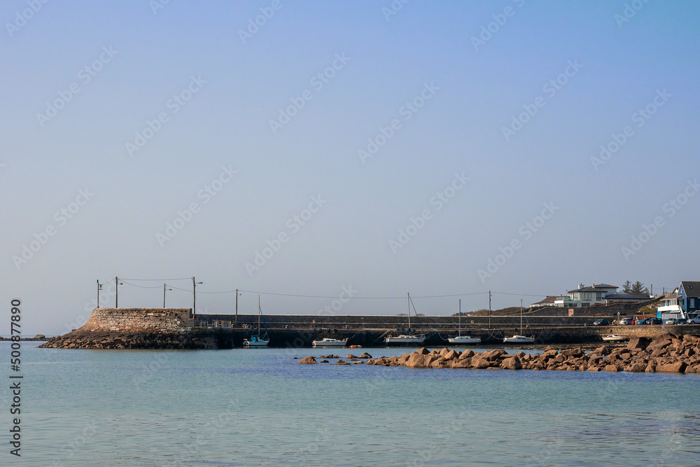 Small stone Barna pier, county Galway, Ireland. Blue ocean and sky. Popular travel area. Irish landscape. Small yachts and fishing boats. Warm sunny day. Small stone Barna pier, county Galway, Ireland. Blue ocean and sky. Popular travel area. Irish landscape. Small yachts and fishing boats. Warm sunny day.