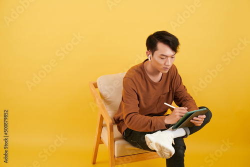 Young graphic designer sitting in armchair and drawing sketch of project on digital tablet