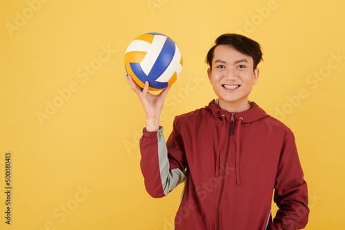Smiling young Vietnamese man holding volleyball ball, isolated on yellow