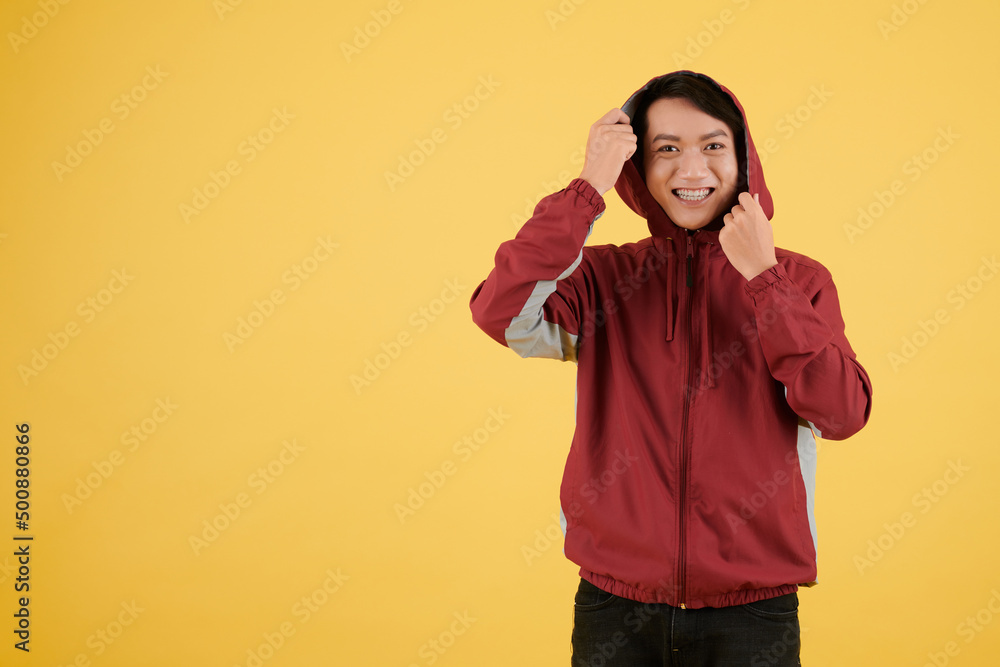 Happy excited young man putting on hood of track jacked, isolated on yellow Happy excited young man putting on hood of track jacked, isolated on yellow