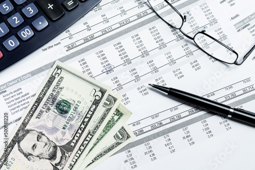 US dollar banknotes, pen, calculator and eyeglasses on a mockup balance sheet. Accounting, business, finance and tax concepts. © Robert