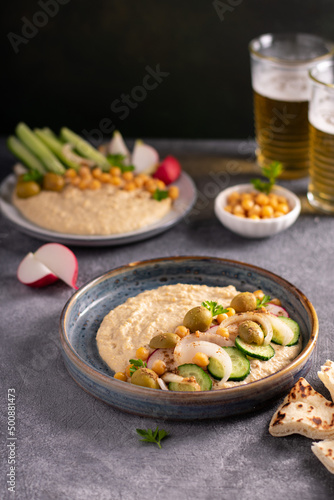 Hummus. two bowls of homemade hummus garnished with chickpeas, olives, parsley and cucumbers. Vertical. Levantine cuisine