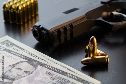 9 mm semi-automatic pistol, full metal jacket bullets and dollar banknotes on black background. Conceptual mockup of gun control, crime, military-industrial complex.