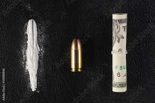 A line of cocaine powder, a single 9 mm bullet and dollar bill scroll. Conceptual mockup of illegal drug dealing, trafficking, war on drugs.