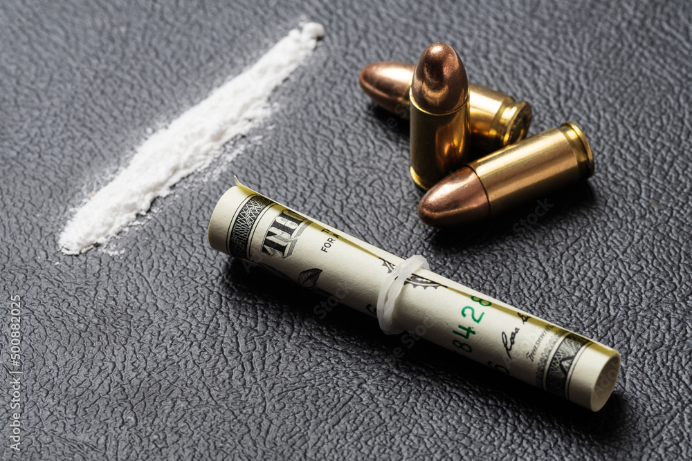Dollar bill scroll, a line of cocaine powder and three 9 mm bullets on black surface. Conceptual mockup of illegal drug dealing, trafficking, war on drugs. Dollar bill scroll, a line of cocaine powder and three 9 mm bullets on black surface. Conceptual mockup of illegal drug dealing, trafficking, war on drugs.
