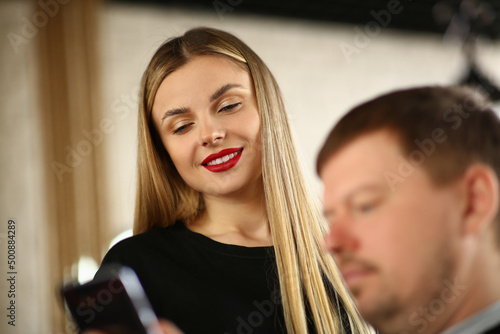 Smiling pretty blonde showing photo in smartphone to man