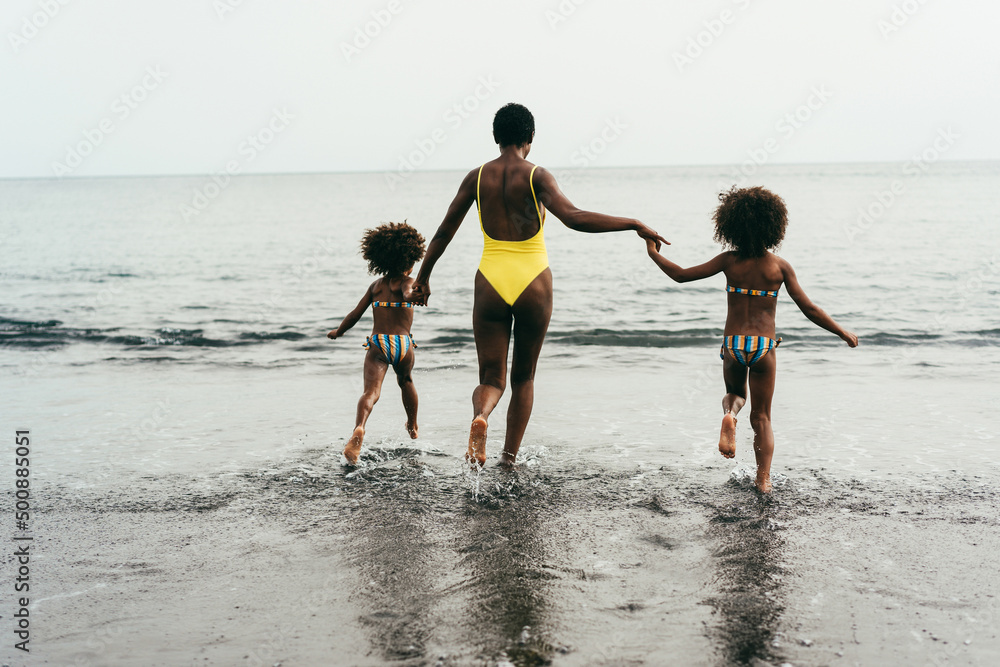 African sisters twins having fun running on the beach with their mother - Main focus on mom head