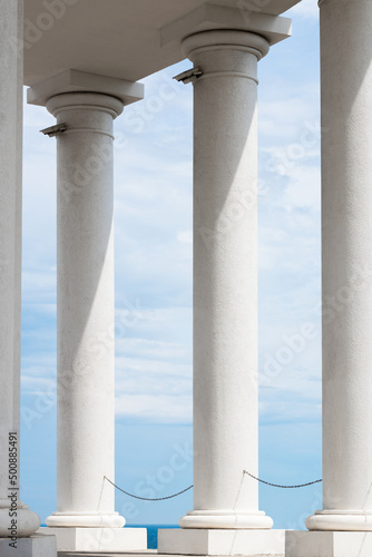 A row of huge white columns with a sky in the clouds in the background