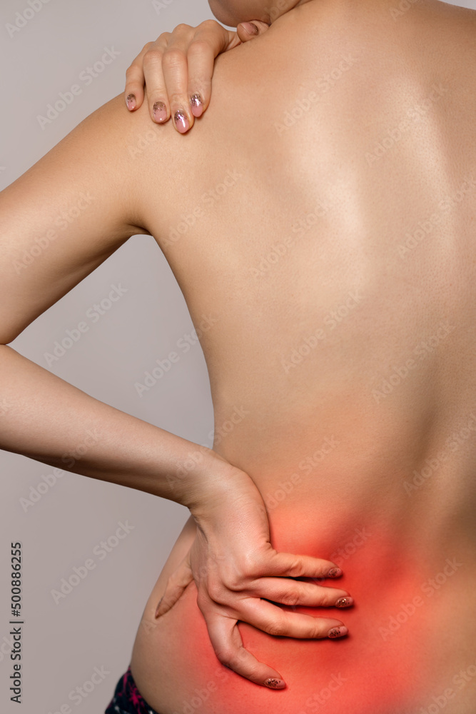 Fototapeta premium Woman having backache, pain back isolated on gray background. Scoliosis. Spinal cord problems on womans back. Woman touching her back.