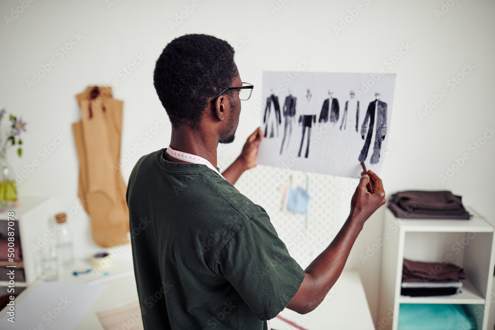 Young Black fashion designer holding sheet of skeches for new collection he created Young Black fashion designer holding sheet of skeches for new collection he created