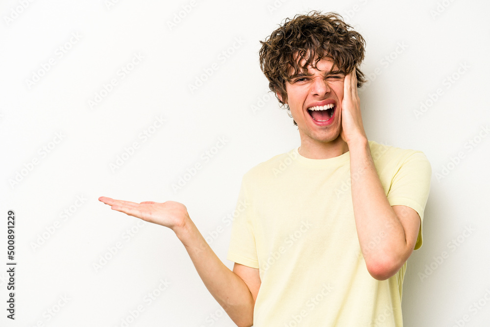 Young caucasian man isolated on white background holds copy space on a palm, keep hand over cheek. Amazed and delighted. Young caucasian man isolated on white background holds copy space on a palm, keep hand over cheek. Amazed and delighted.