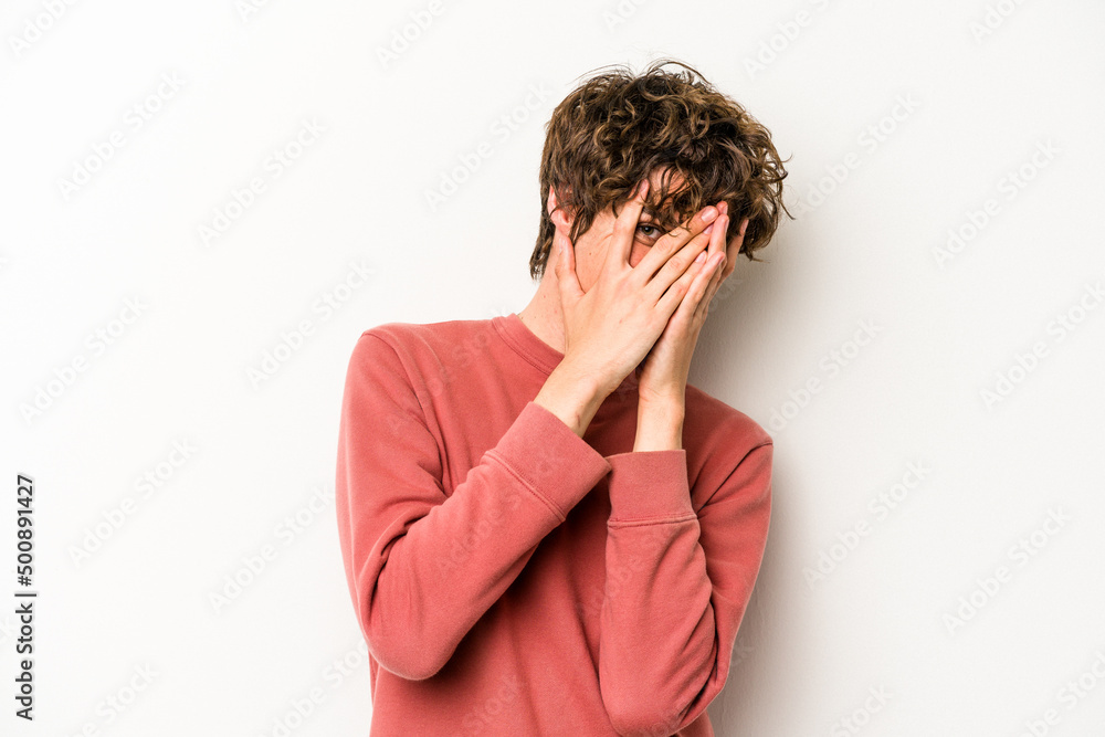 Young caucasian man isolated on white background blink at the camera through fingers, embarrassed covering face. Young caucasian man isolated on white background blink at the camera through fingers, embarrassed covering face.