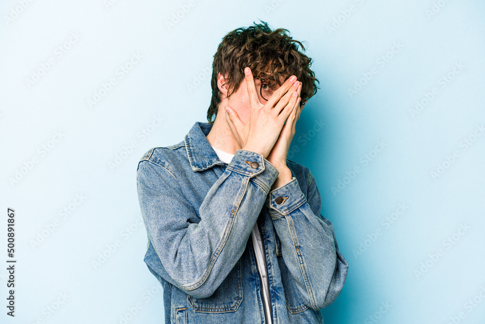 Young caucasian man isolated on blue background blink through fingers frightened and nervous. Young caucasian man isolated on blue background blink through fingers frightened and nervous.