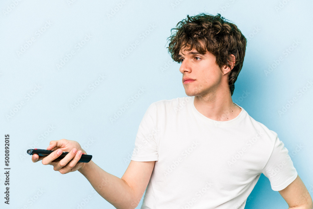 Young caucasian man holding tv controller isolated on blue background Young caucasian man holding tv controller isolated on blue background