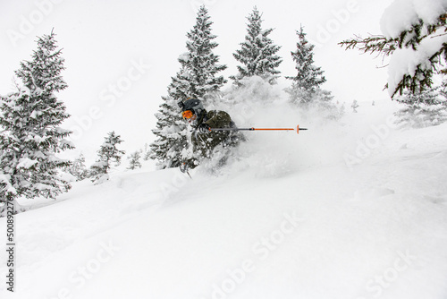 Canvas skier descending a snow-covered mountain slope and splash of snow around him