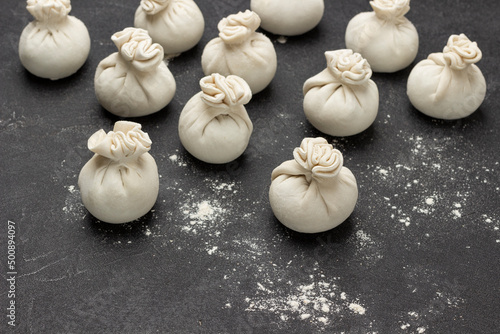 Raw khinkali dumplings and flour on table.