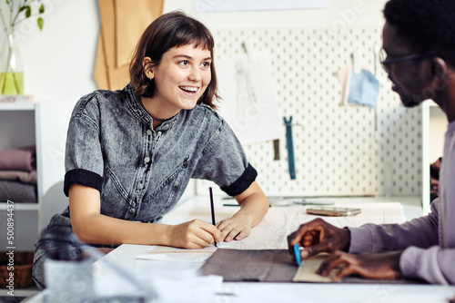 Excited young female fashion designer drawing sewing pattern and talking to coworker photo