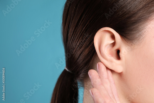 Woman showing hand to ear gesture on light blue background, closeup. Space for text photo