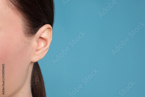 Woman on light blue background, closeup of ear. Space for text photo