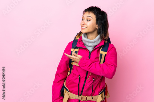 Young mountaineer girl with a big backpack over isolated pink background extending hands to the side for inviting to come