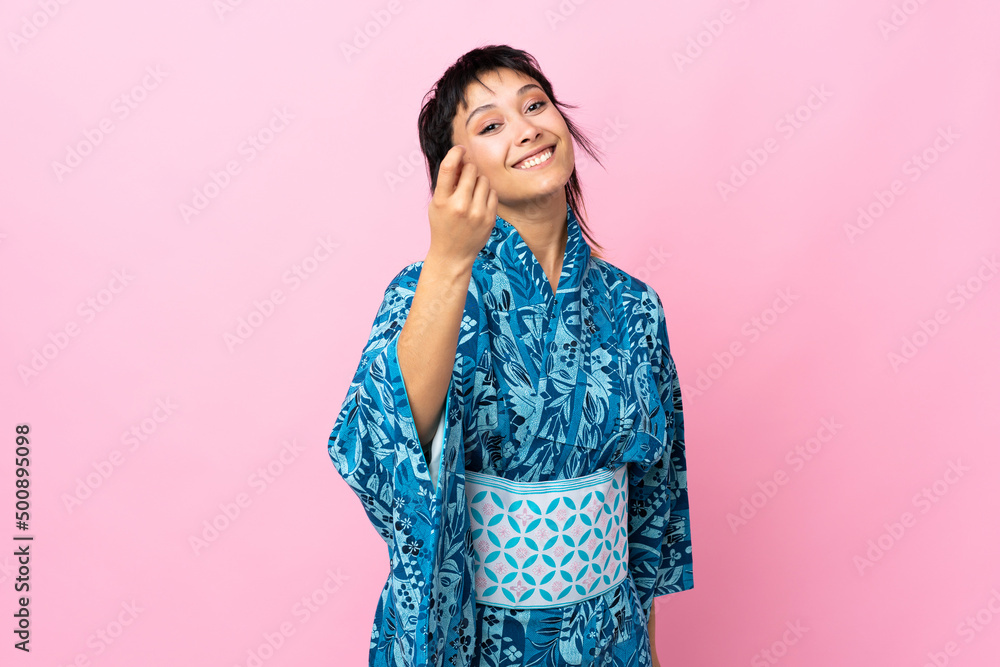 Young woman wearing kimono over isolated blue background making money gesture Young woman wearing kimono over isolated blue background making money gesture