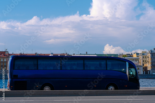 A modern blue bus rides through a European city. Tourist bus rides along the embankment.