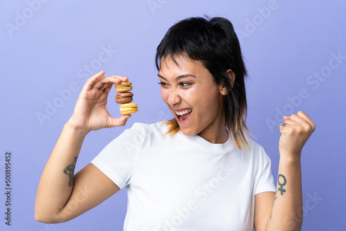 Young Uruguayan woman over isolated purple background holding colorful French macarons and celebrating a victory