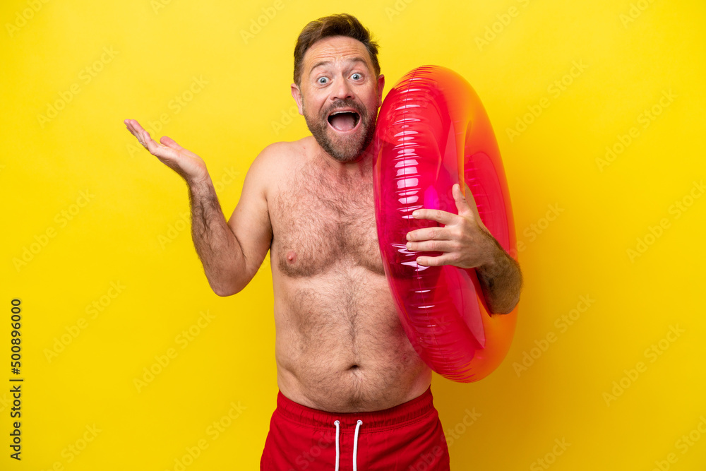 Middle age caucasian man holding inflatable donut isolated on yellow background with shocked facial expression