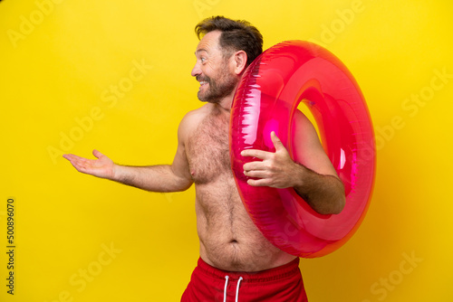 Middle age caucasian man holding inflatable donut isolated on yellow background with surprise expression while looking side