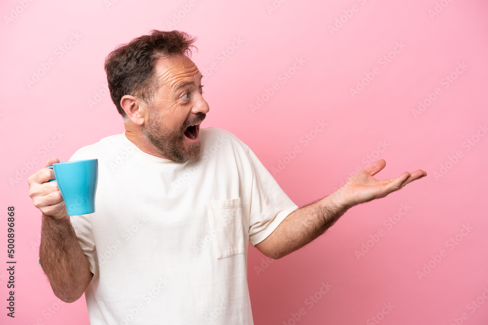 Middle age caucasian man holding cup of coffee isolated on pink background with surprise facial expression