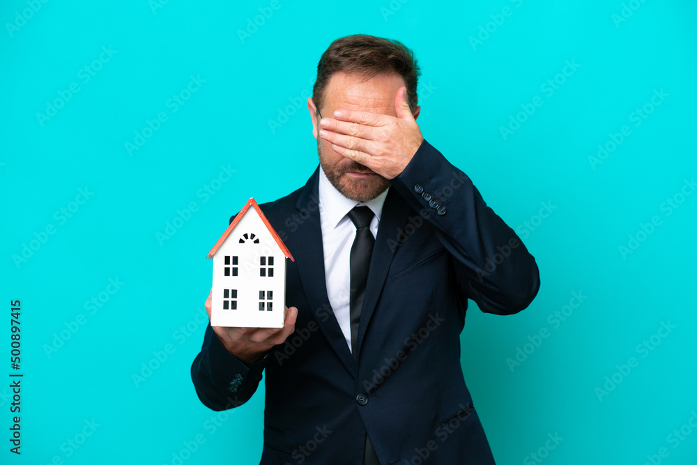 Real estate middle age agent man isolated on blue background covering eyes by hands. Do not want to see something Real estate middle age agent man isolated on blue background covering eyes by hands. Do not want to see something