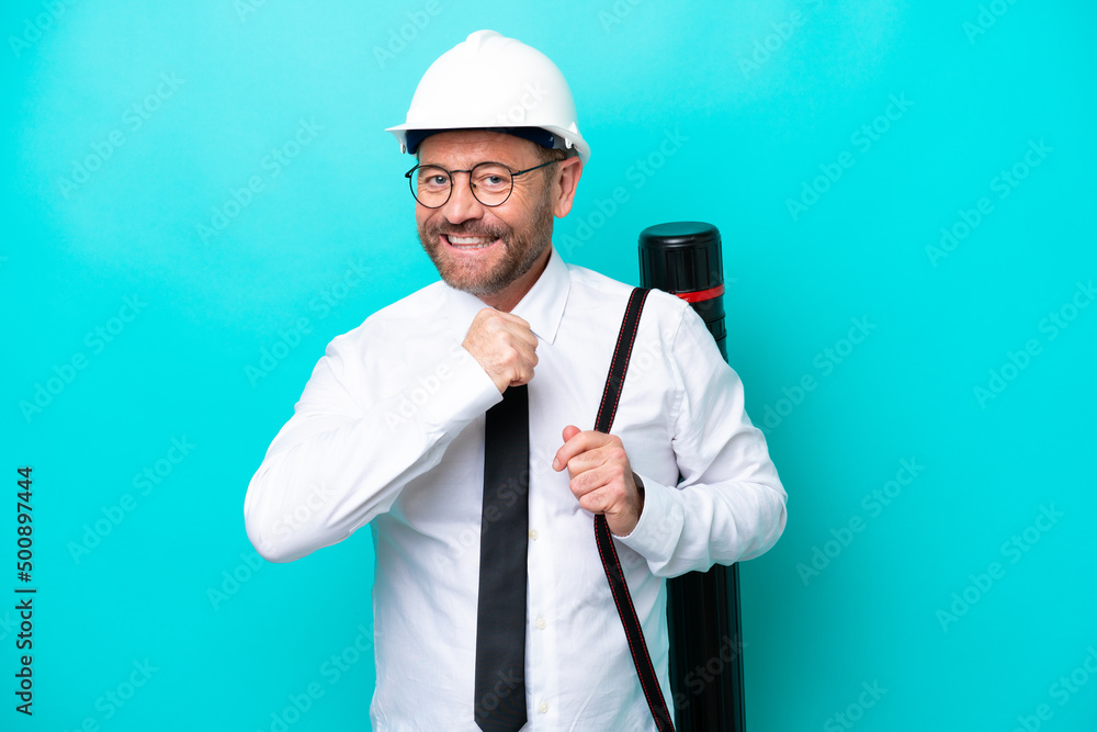 Middle age architect man with helmet and holding blueprints isolated on blue background celebrating a victory Middle age architect man with helmet and holding blueprints isolated on blue background celebrating a victory