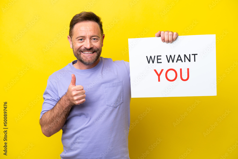 Middle age caucasian man isolated on yellow background holding We Want You board with thumb up Middle age caucasian man isolated on yellow background holding We Want You board with thumb up