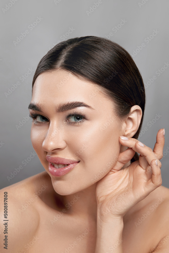 Beauty face. Woman with natural makeup and healthy skin portrait. Beautiful girl model touching fresh facial skin on grey background closeup. Skin care concept