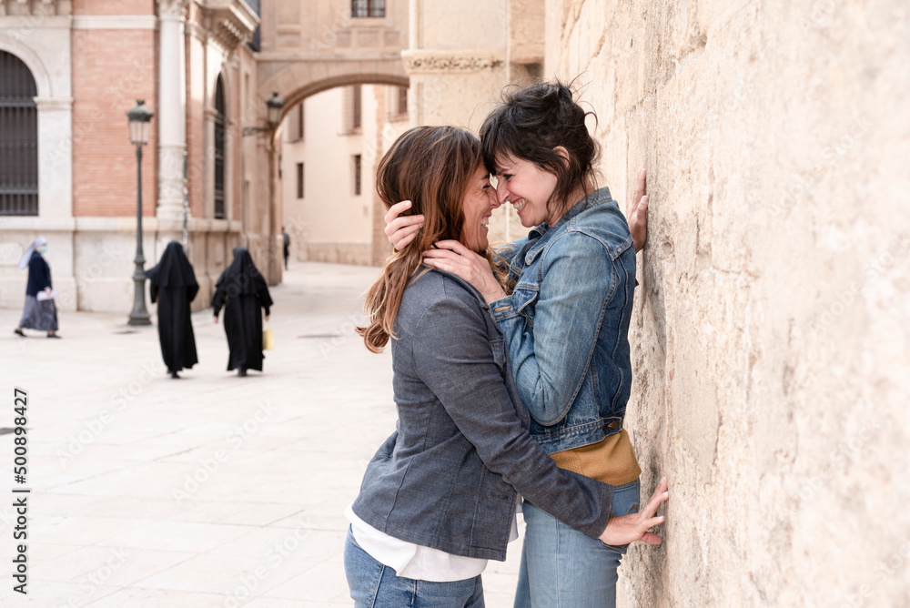 young lesbian couple laughing and hugging in the streets of Valencia, nuns in the background, gay concept young lesbian couple laughing and hugging in the streets of Valencia, nuns in the background, gay concept