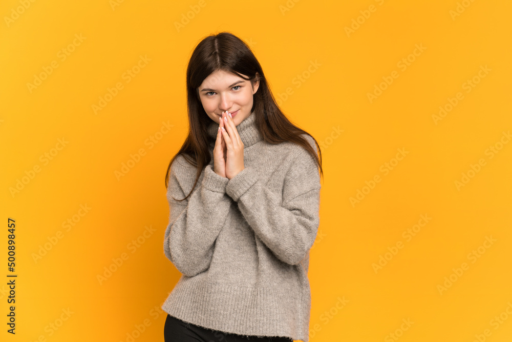 Young Ukrainian girl isolated on yellow background keeps palm together. Person asks for something Young Ukrainian girl isolated on yellow background keeps palm together. Person asks for something