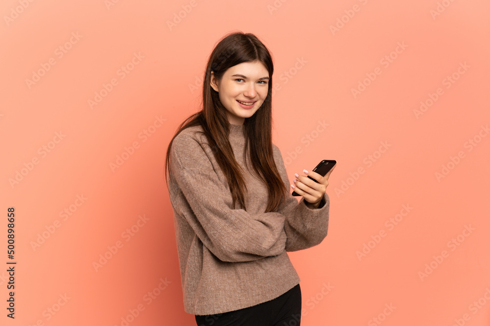 Young Ukrainian girl isolated on pink background holding a mobile phone and with arms crossed Young Ukrainian girl isolated on pink background holding a mobile phone and with arms crossed