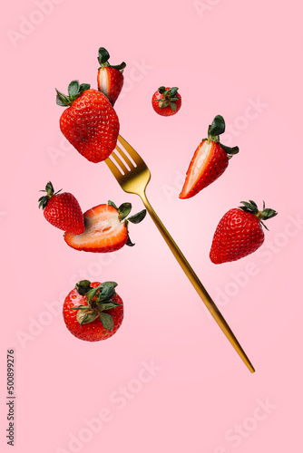 Foto Fresh strawberries thrown in the air, with golden fork, flying and levitating on a bright pink background