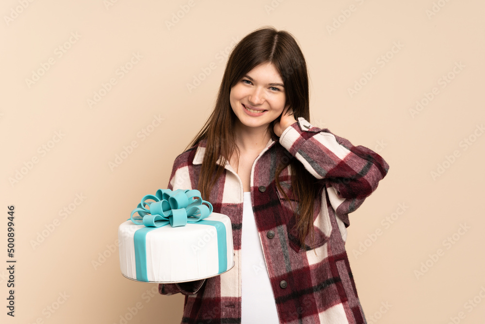 Young Ukrainian girl holding a big cake isolated on beige background laughing Young Ukrainian girl holding a big cake isolated on beige background laughing