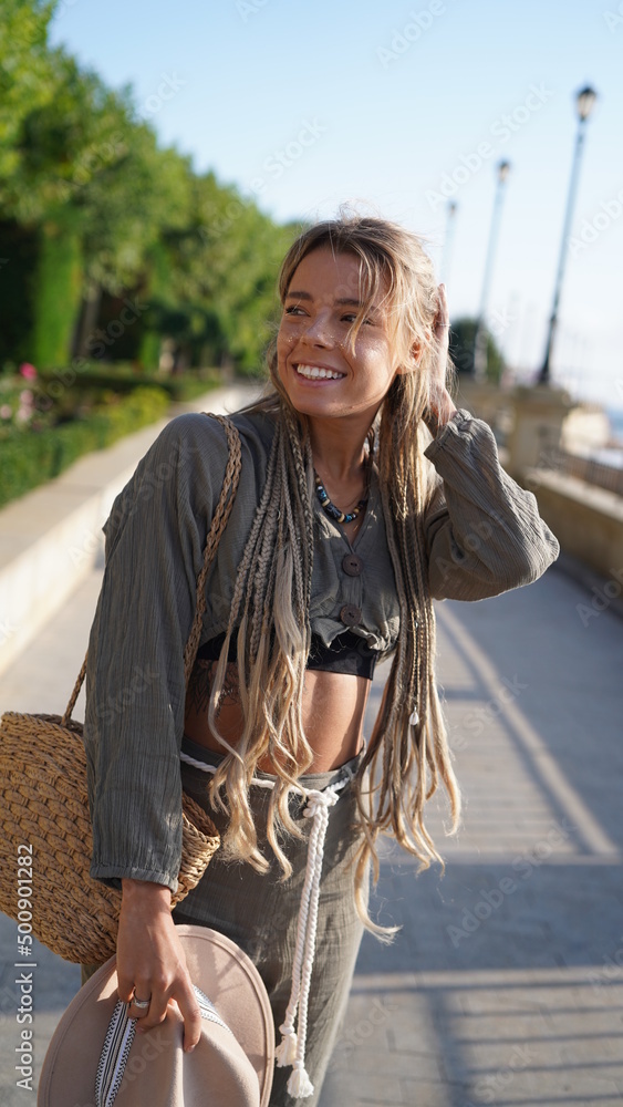 Portrait of a smiling girl with dreadlocks. Bohemian woman in boho style holding a hat. A charming girl with freckles in a hat smiles and laughs merrily. Bright and beautiful smile, street style.
