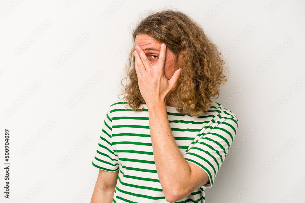 Young caucasian man isolated on white background blink at the camera through fingers, embarrassed covering face. Young caucasian man isolated on white background blink at the camera through fingers, embarrassed covering face.