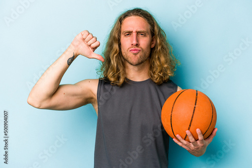 Young caucasian man playing basketball isolated on blue background feels proud and self confident, example to follow.