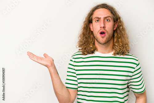 Young caucasian man isolated on white background impressed holding copy space on palm.