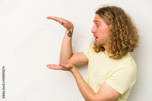 Young caucasian man isolated on white background shocked and amazed holding a copy space between hands.