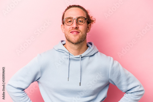 Young caucasian man isolated on pink background confident keeping hands on hips.
