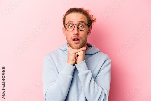 Young caucasian man isolated on pink background praying for luck, amazed and opening mouth looking to front.