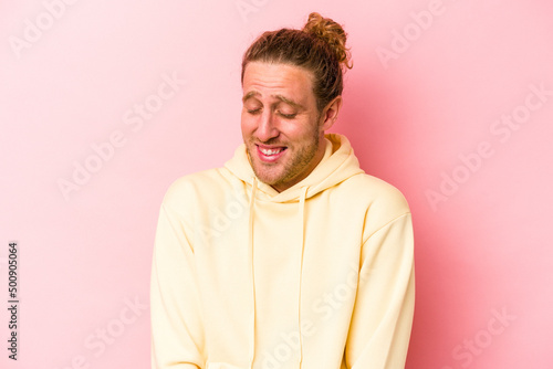 Young caucasian man isolated on pink background laughs and closes eyes, feels relaxed and happy.